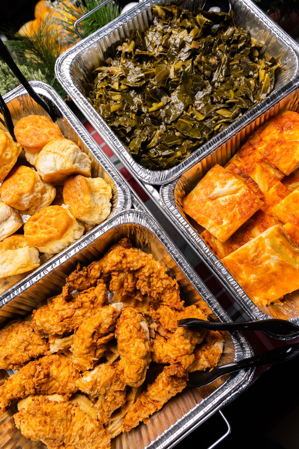 Overhead shot of chicken, greens, and biscuits in catering tins