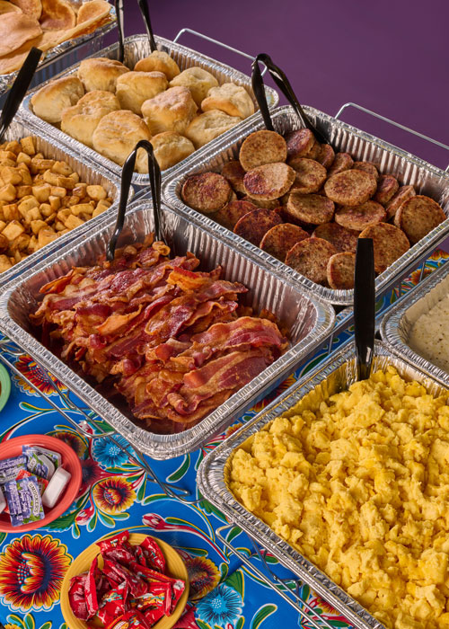 Overhead shot of bacon, scrambled eggs, sausage, potatoes and biscuits catering buffet spread