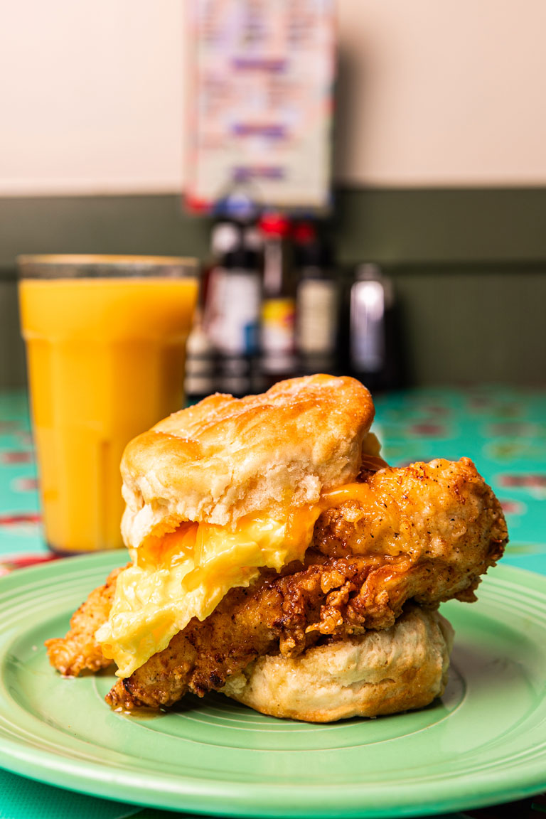 Side Profile of Chicken Biscuit with Glass of Orange Juice in the background.